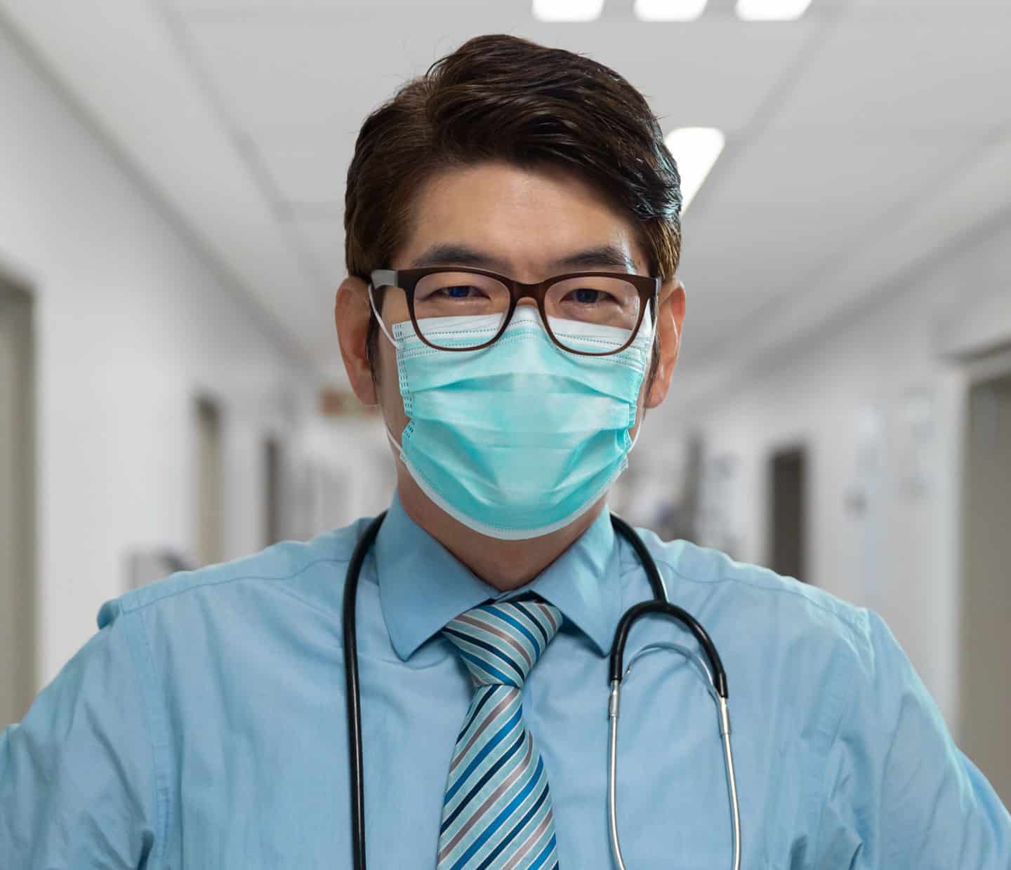 Portrait of mixed race male doctor wearing face mask standing in hospital corridor