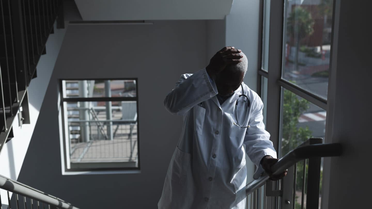 Médecin afro-américain montant l'escalier de l'hôpital en se tenant la tête et en s'inquiétant.