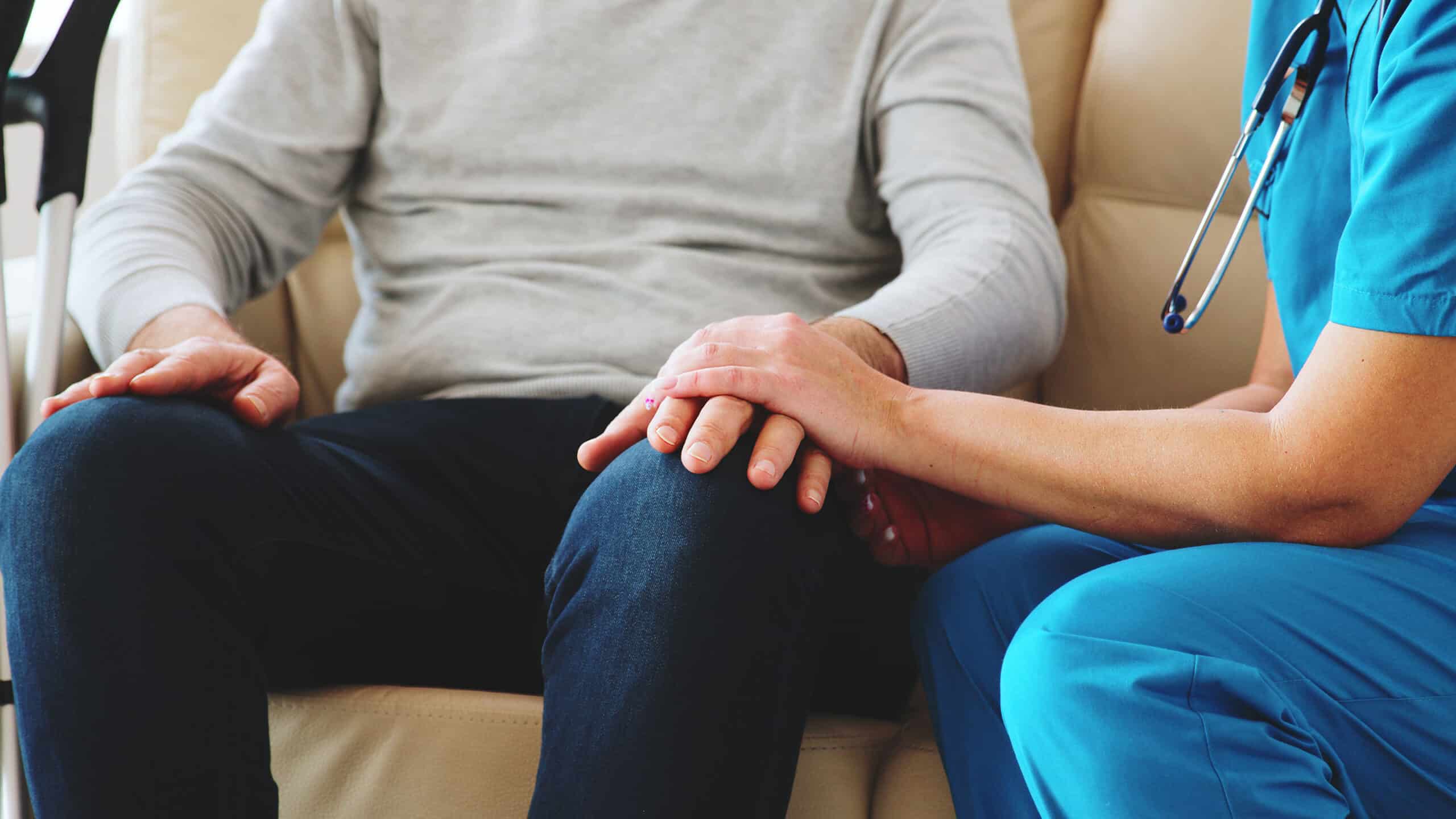 Close up shot of female nurse taking an old man hand while they are sitting on the couch