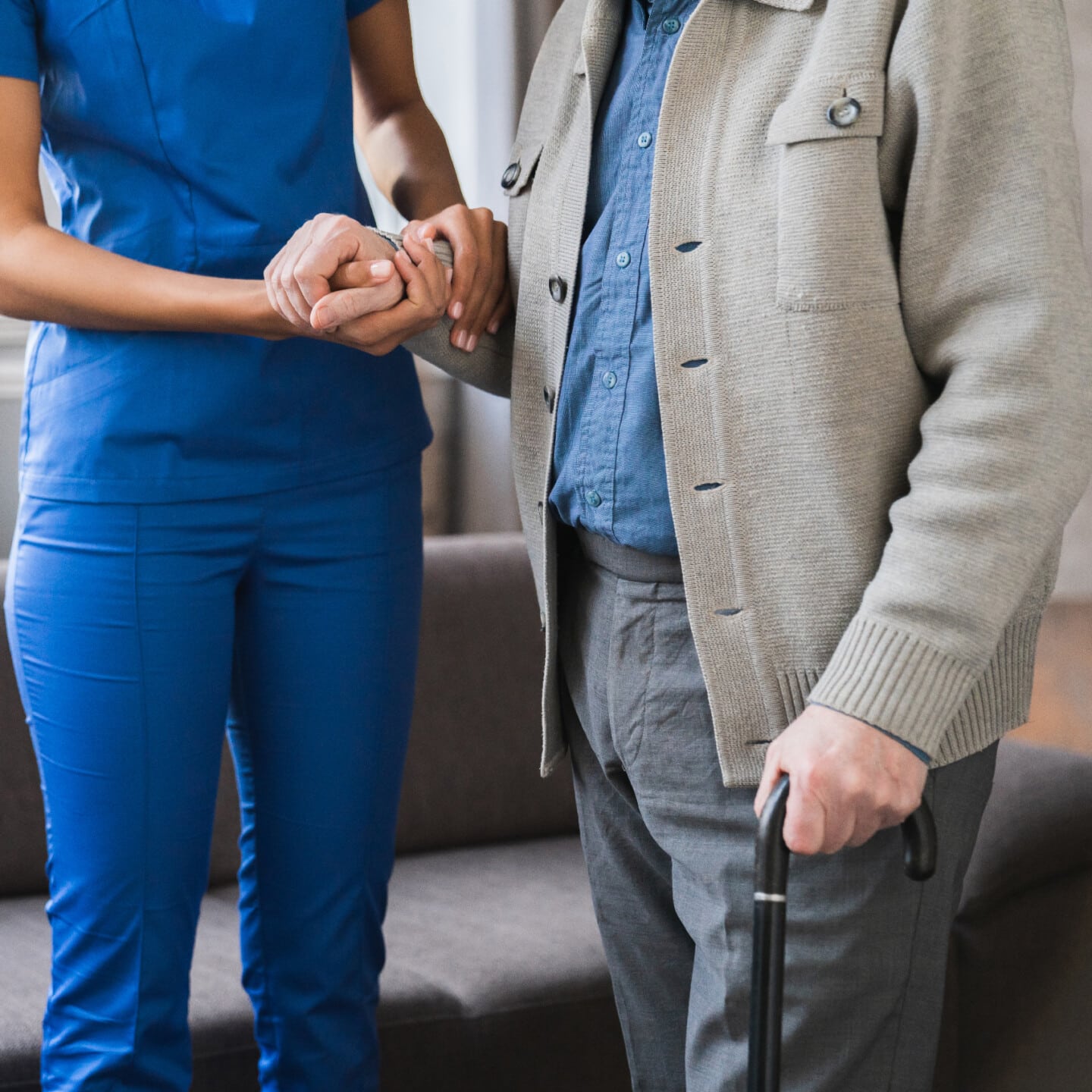 Cropped shot of a senior man with a walking stick being comforted by nurse in the hospice.Care worker helping to elderly patients to walk in geriatric clinic.