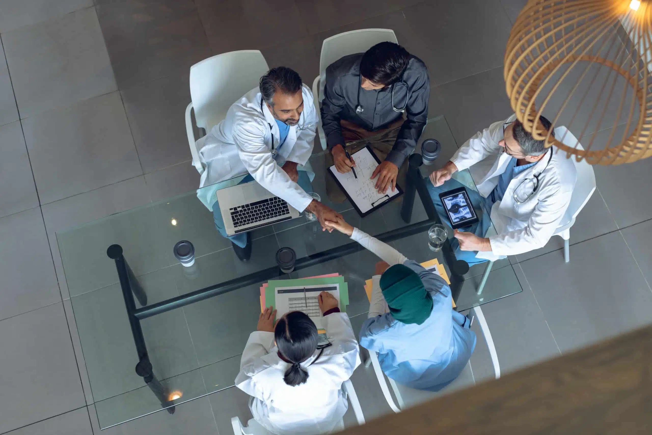 Vue en plongée d'une équipe médicale travaillant ensemble à une table dans un hôpital. Une tasse à café, des dossiers médicaux, un presse-papiers, une tablette numérique et un ordinateur portable sont posés sur la table.