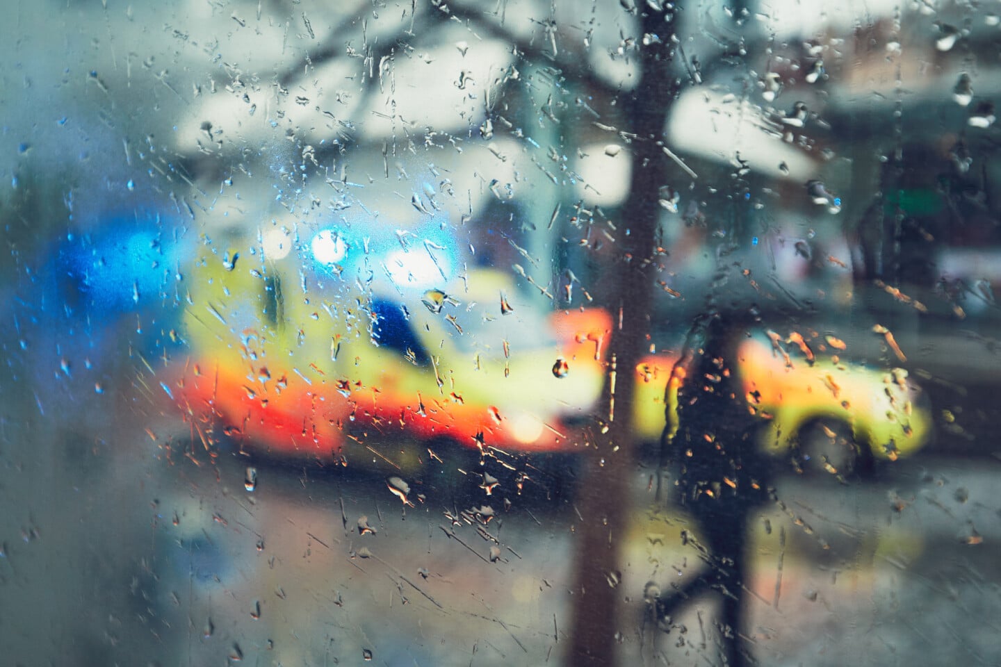 Emergency medical service response in the city. Ambulance cars on the rush street during rain. View through a car window and selective focus on the raindrop. Prague, Czech Republic.