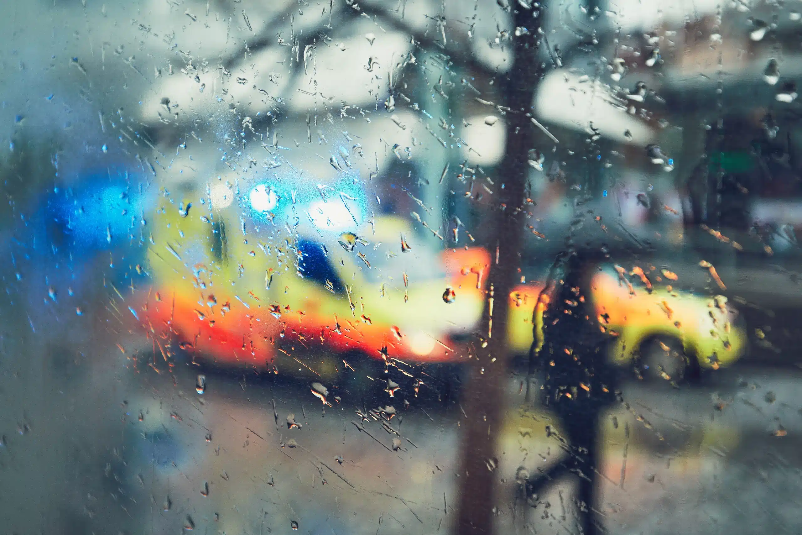 Emergency medical service response in the city. Ambulance cars on the rush street during rain. View through a car window and selective focus on the raindrop. Prague, Czech Republic.