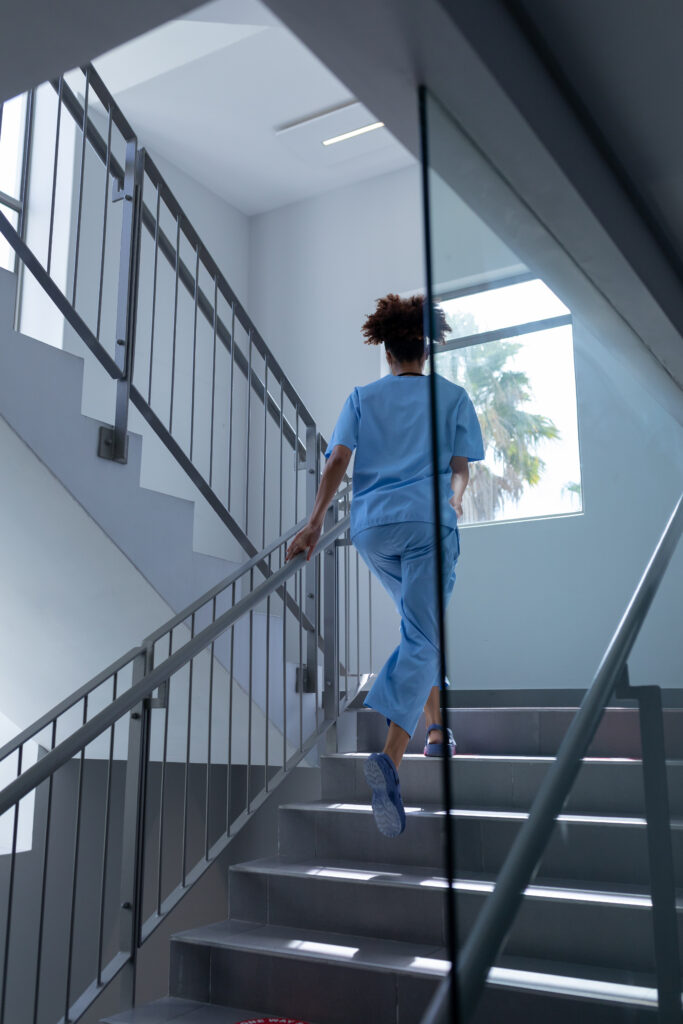 Rear view of mixed race female doctor wearing scrubs running up stairs in hospital. medical professional at work